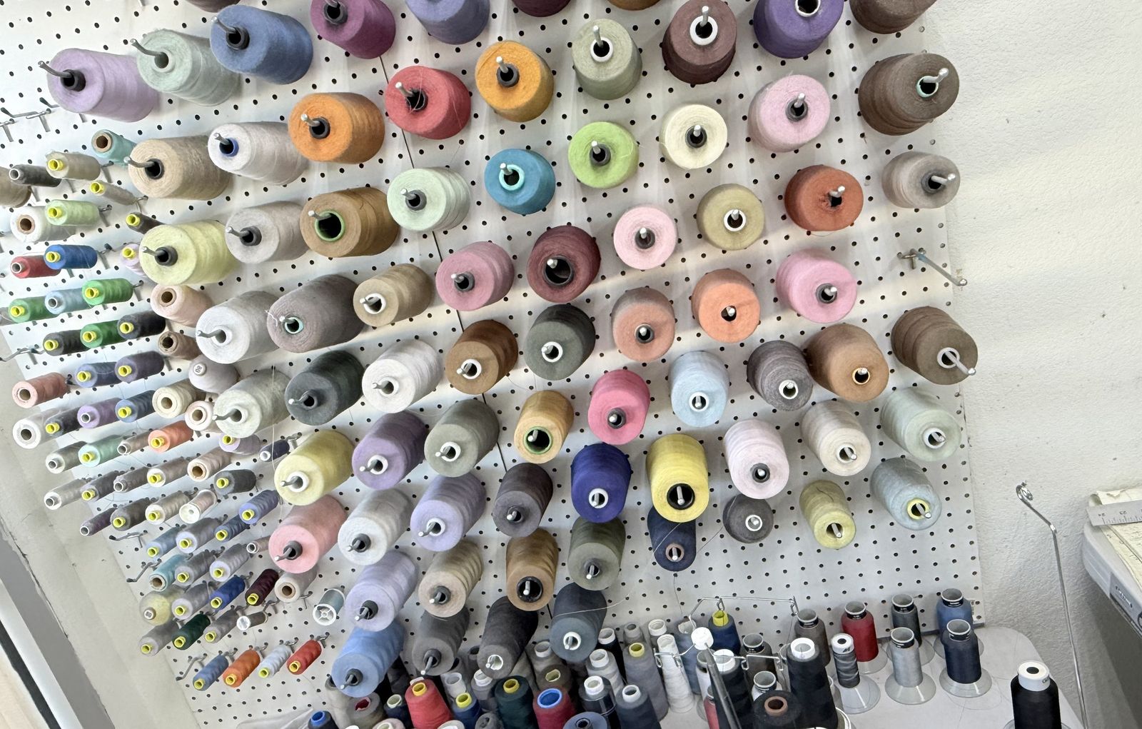 Wall of colorful thread spools above sewing machines in the alterations area